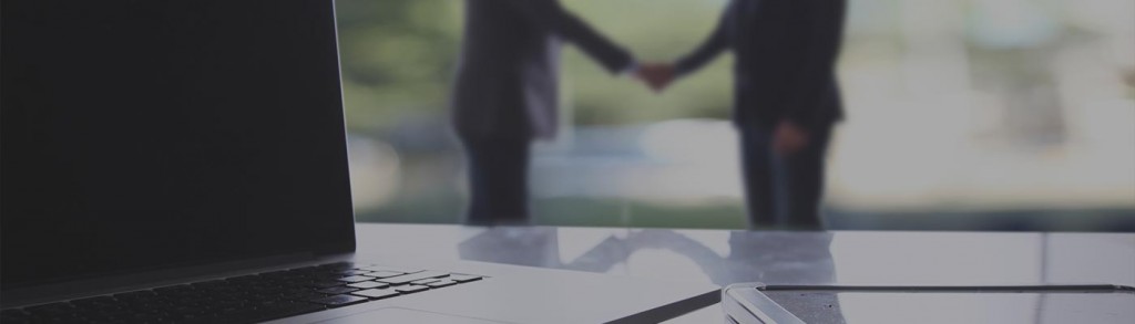Two business men shaking hands behind a laptop