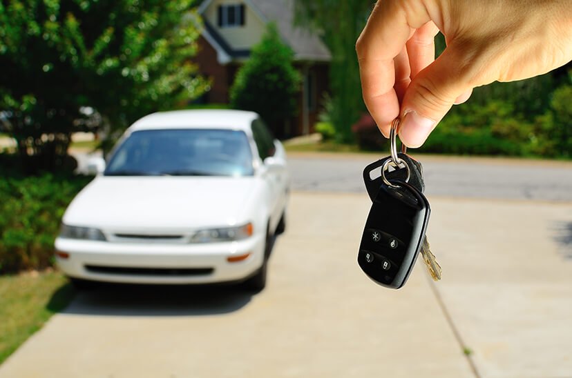 Man Holding Key In Front Of White Car