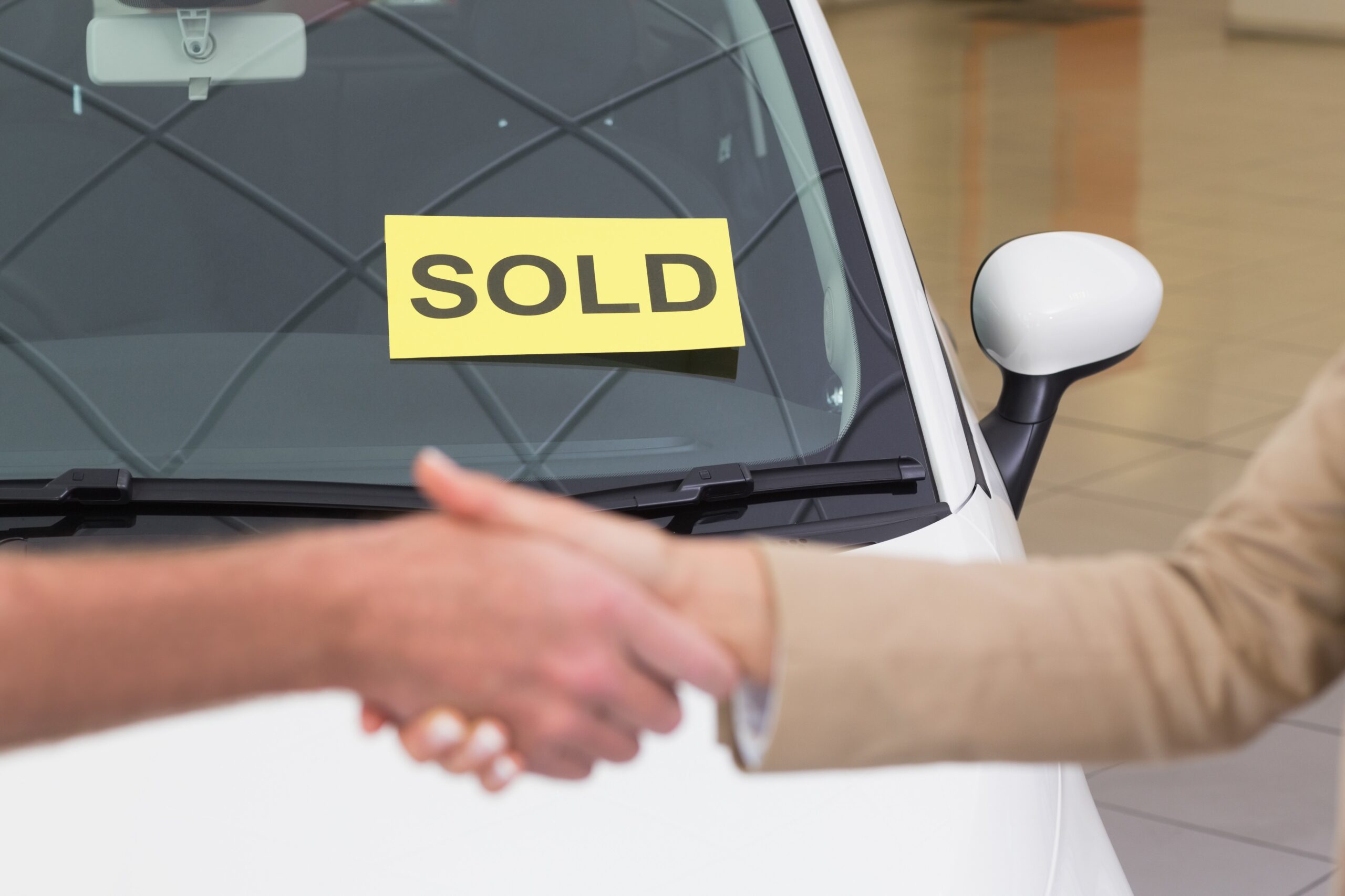 Two People Handshaking In Front Of Vehicle With Sold Sign On Windshield