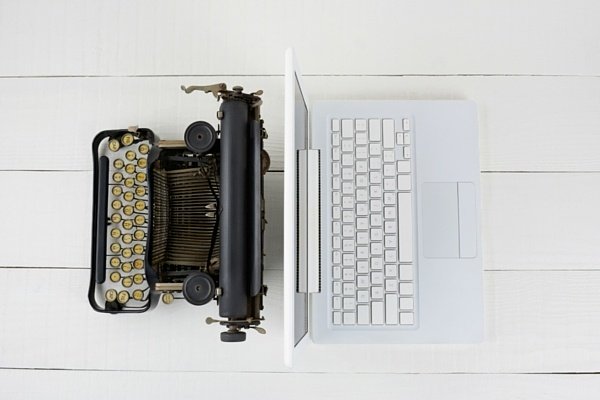 A Laptop And Typewriter Facing Opposite Ways On White Wooden Table