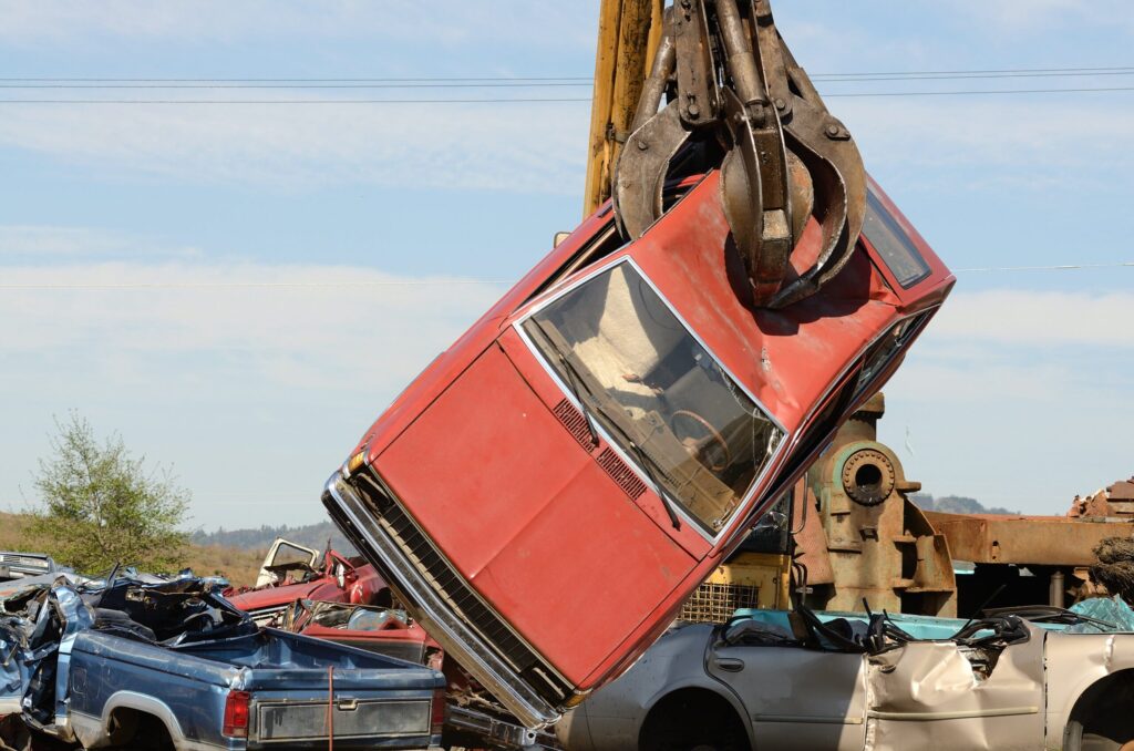 car being moved by crane in junkyard