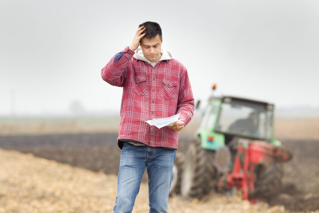 worried man looking at paperwork in field