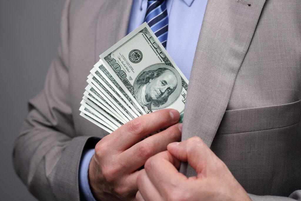 man putting stack of one hundred dollar bills in suit pocket