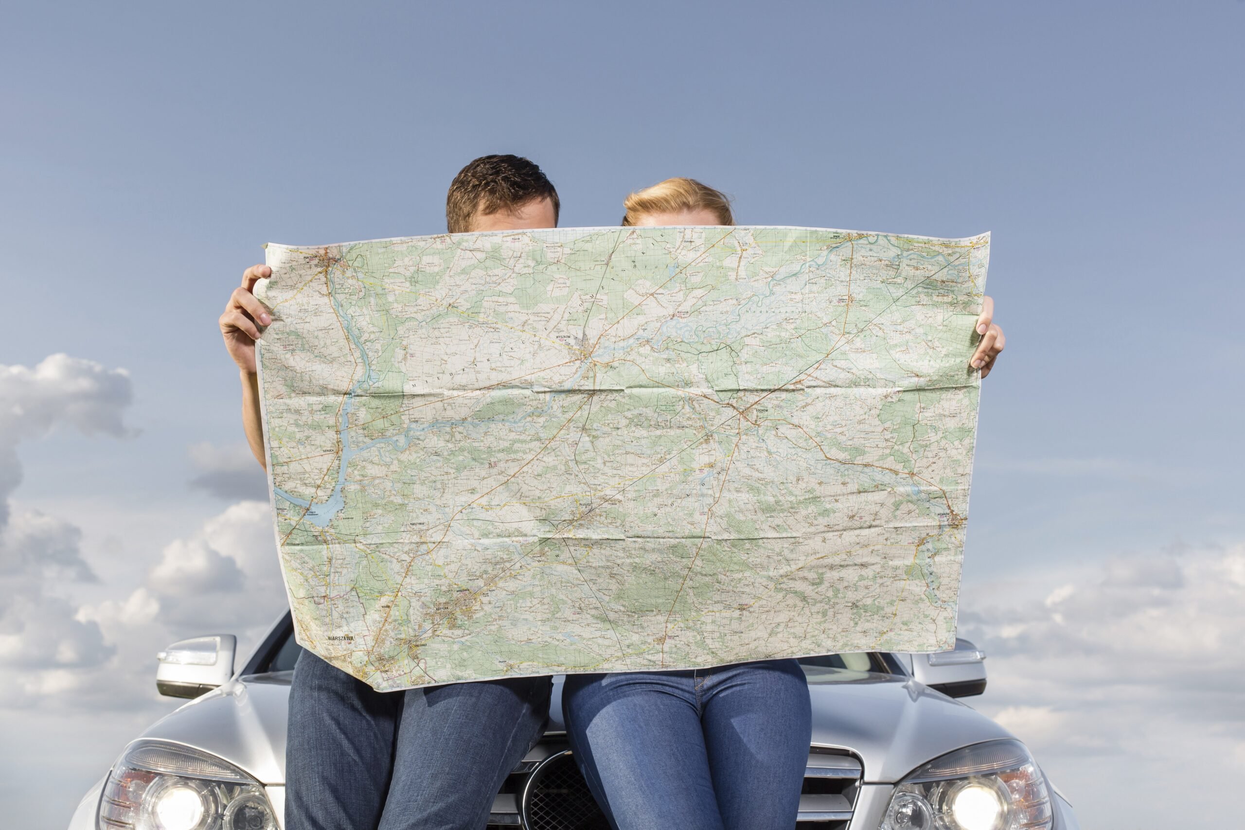 Couple Sitting On Hood Of Car Looking At Map