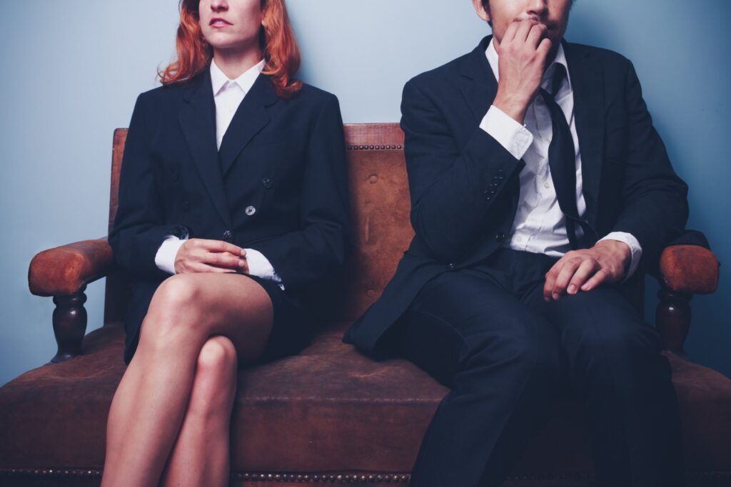 businesswoman and nervous businessman sitting next to each other on bench