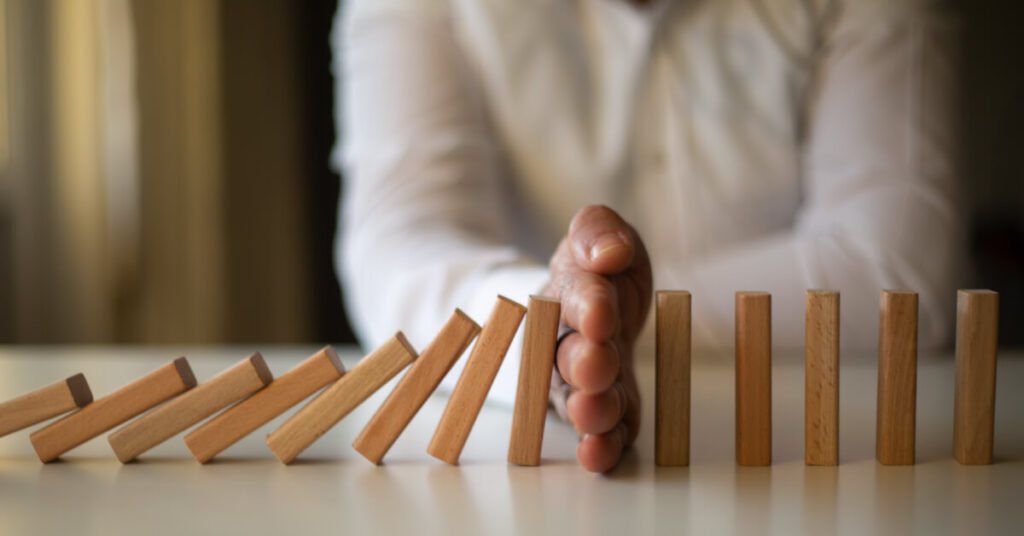 man using hand to stop dominoes from falling